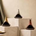 Three chimney-form ceramic incense burners in Ochre, Stone Grey and Rust displayed on tiered limestone blocks.