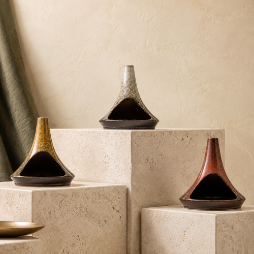 Three chimney-form ceramic incense burners in Ochre, Stone Grey and Rust displayed on tiered limestone blocks.