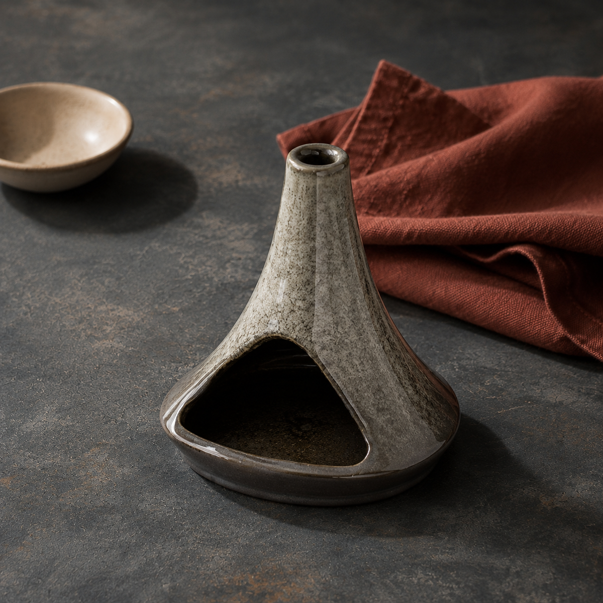 Stone Grey chimney-form ceramic incense burner on charcoal stone beside rust-coloured linen.