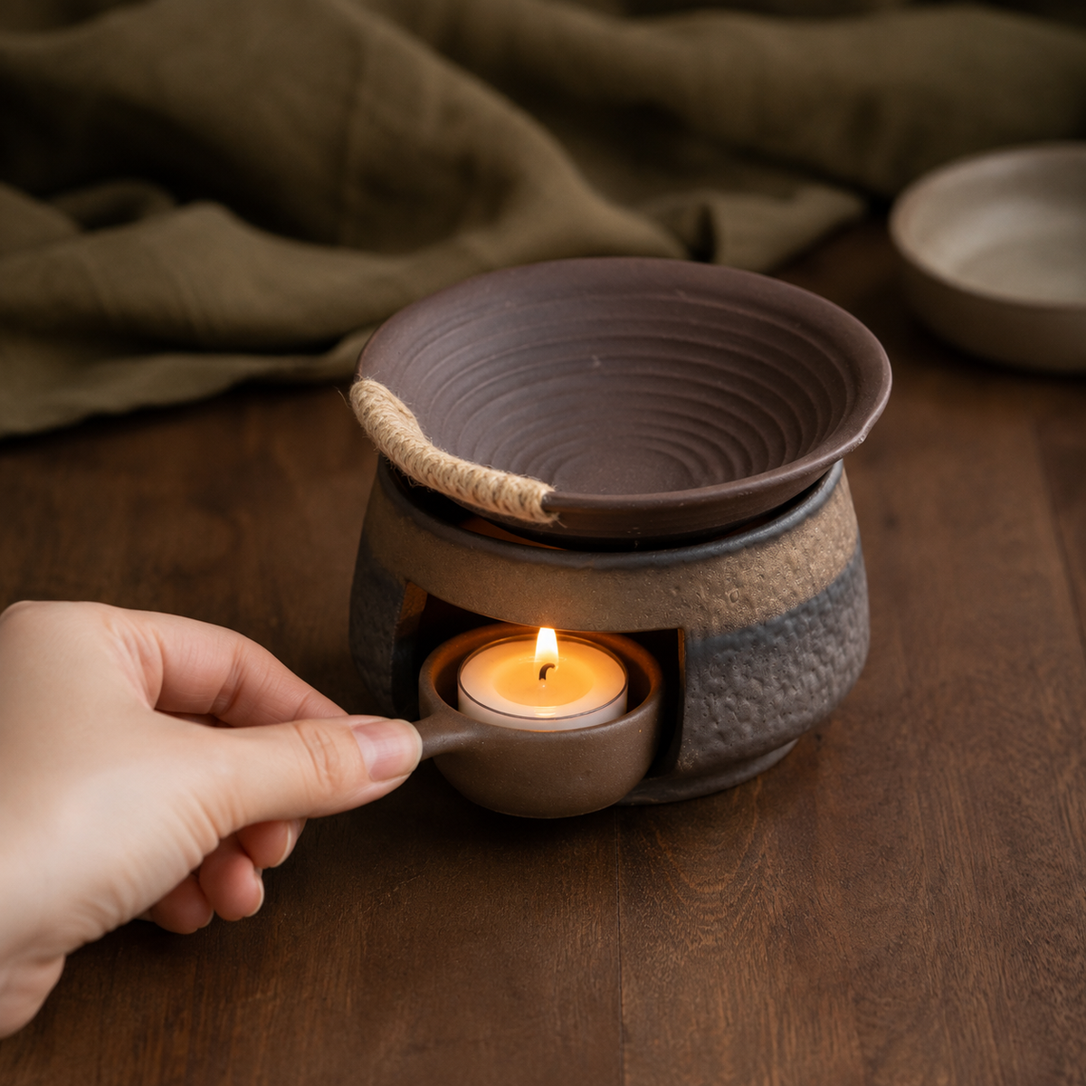 Hand placing a lit tealight cradle inside the ceramic warmer base.