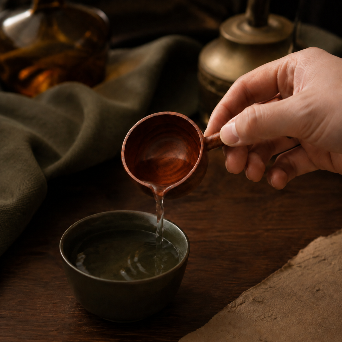Petite acacia wood scoop pouring water into a dark olive cup.