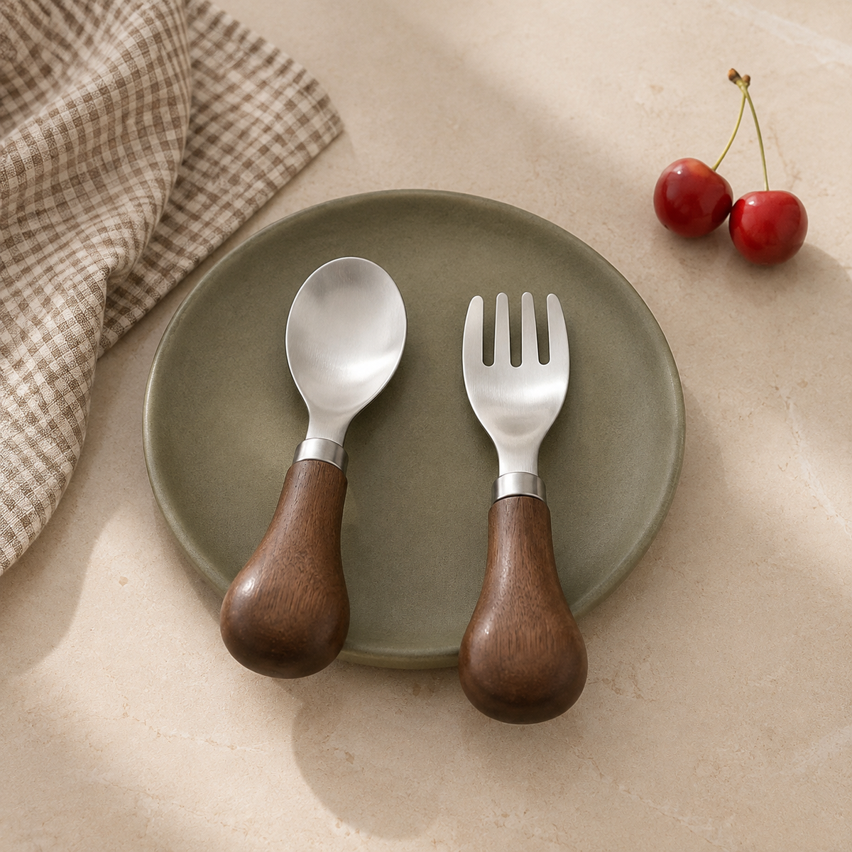 Petite walnut-handled spoon and fork arranged on an olive green plate with cherries.