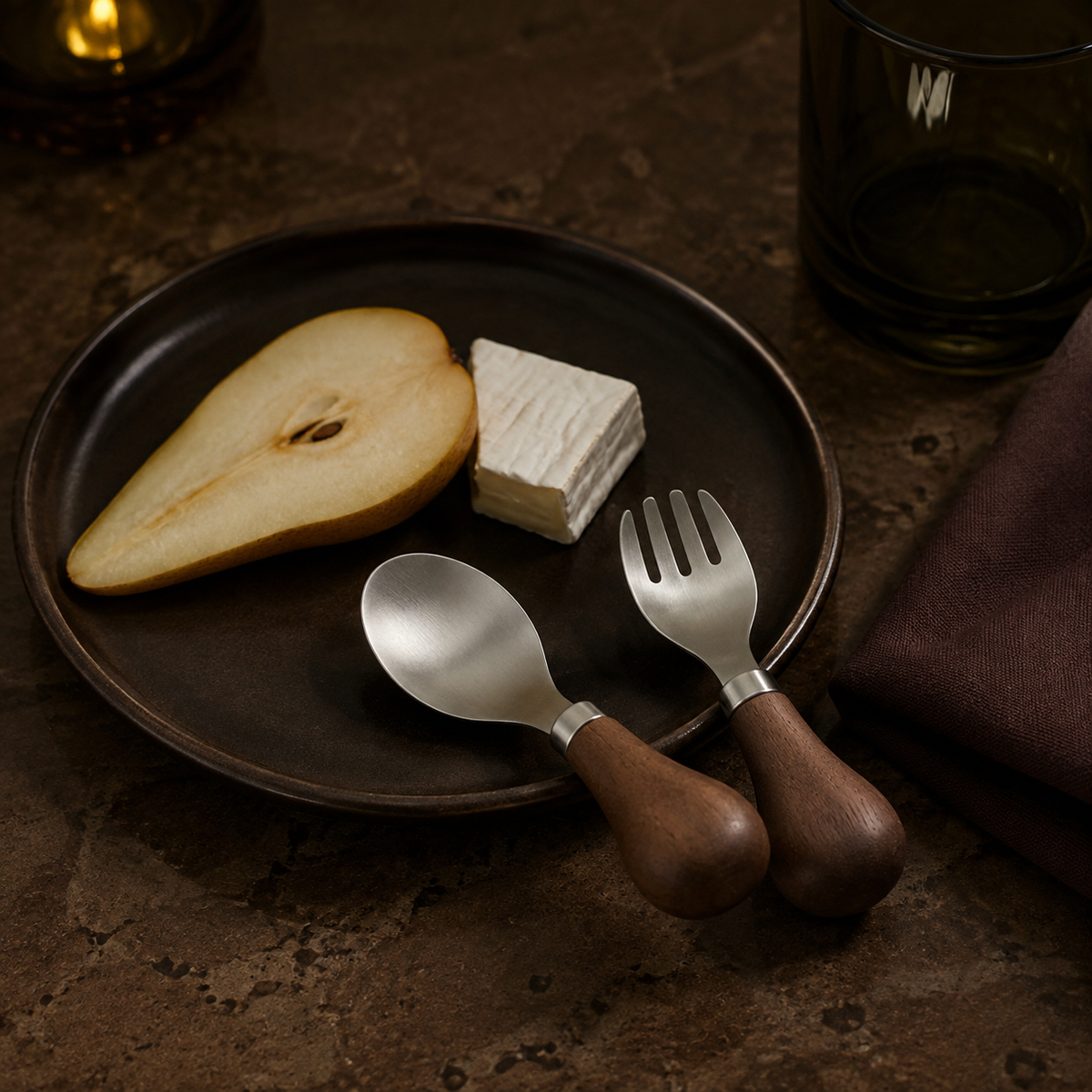Petite walnut-handled spoon and fork styled with pear and cheese on a dark dessert plate.