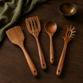 Four individually selectable teak cooking utensils styled on dark walnut with olive linen.