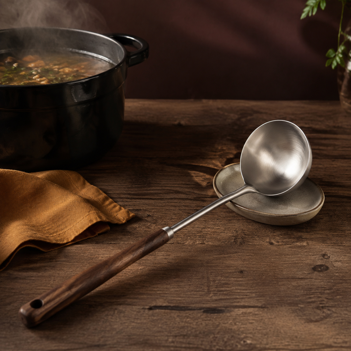 Walnut-handled stainless steel ladle resting beside a steaming soup pot on a dark wooden table.