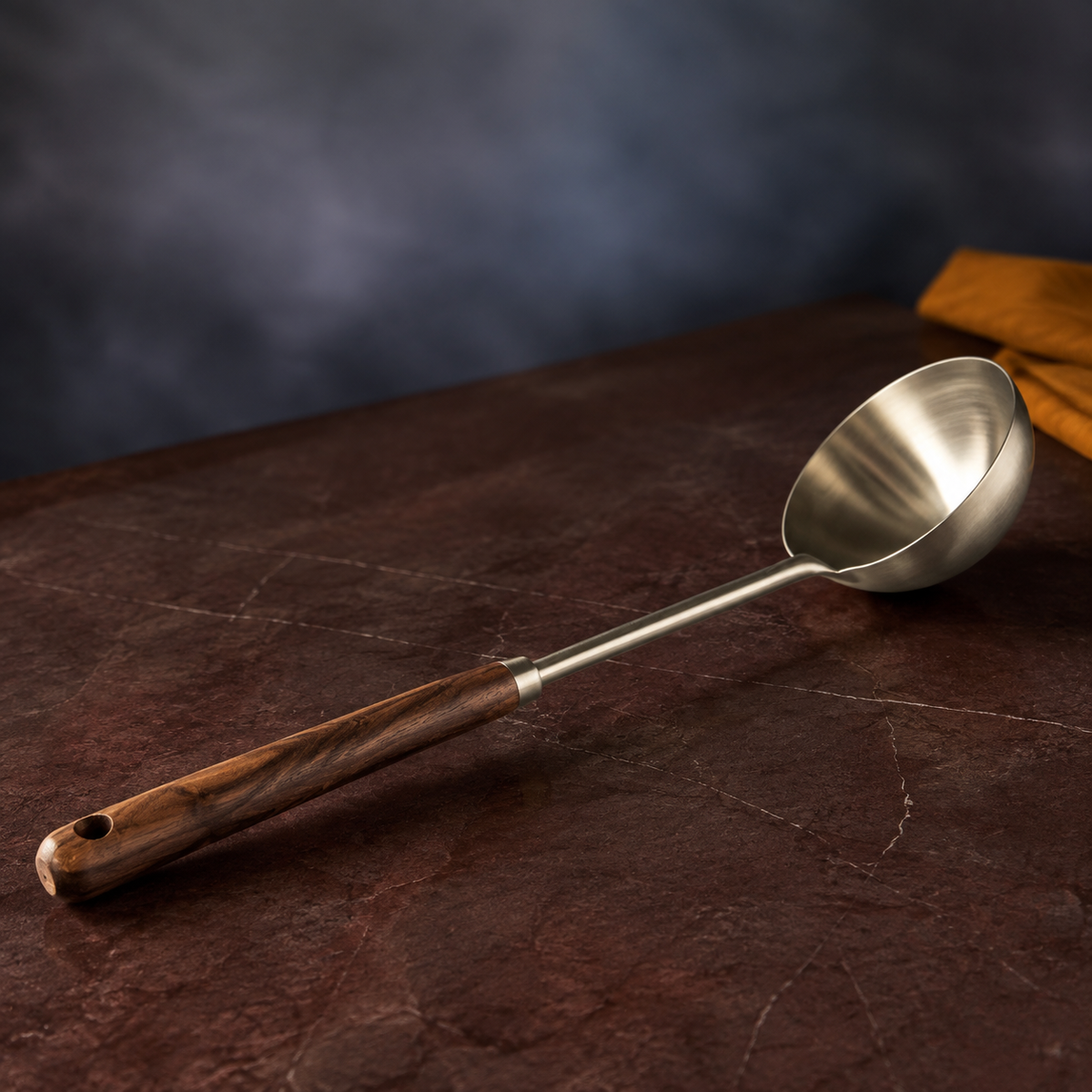 Three-quarter view of a long walnut-handled ladle showing the wood grain, steel collar and deep brushed bowl.