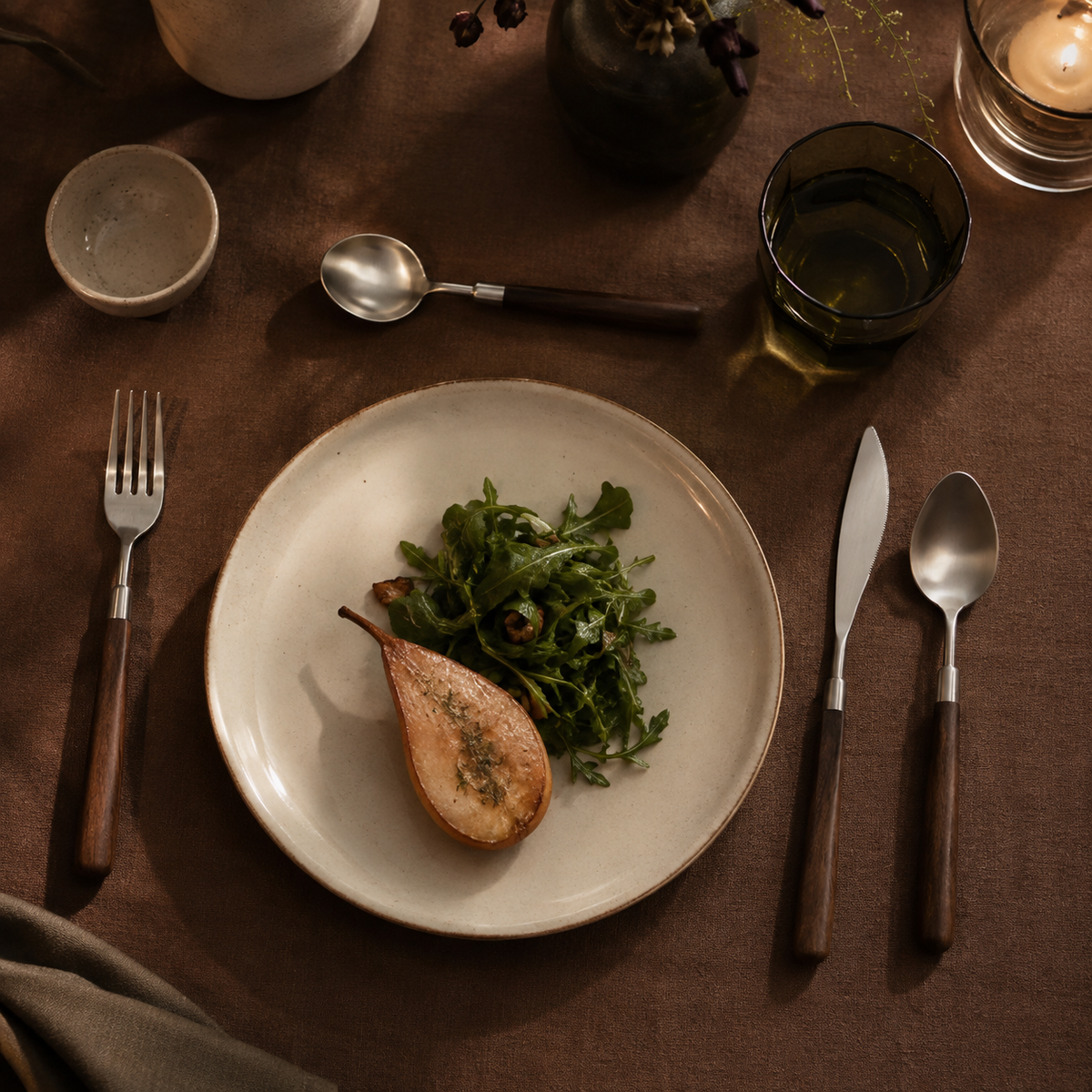 Four-piece walnut-handled flatware set arranged around a warm cream dinner plate.